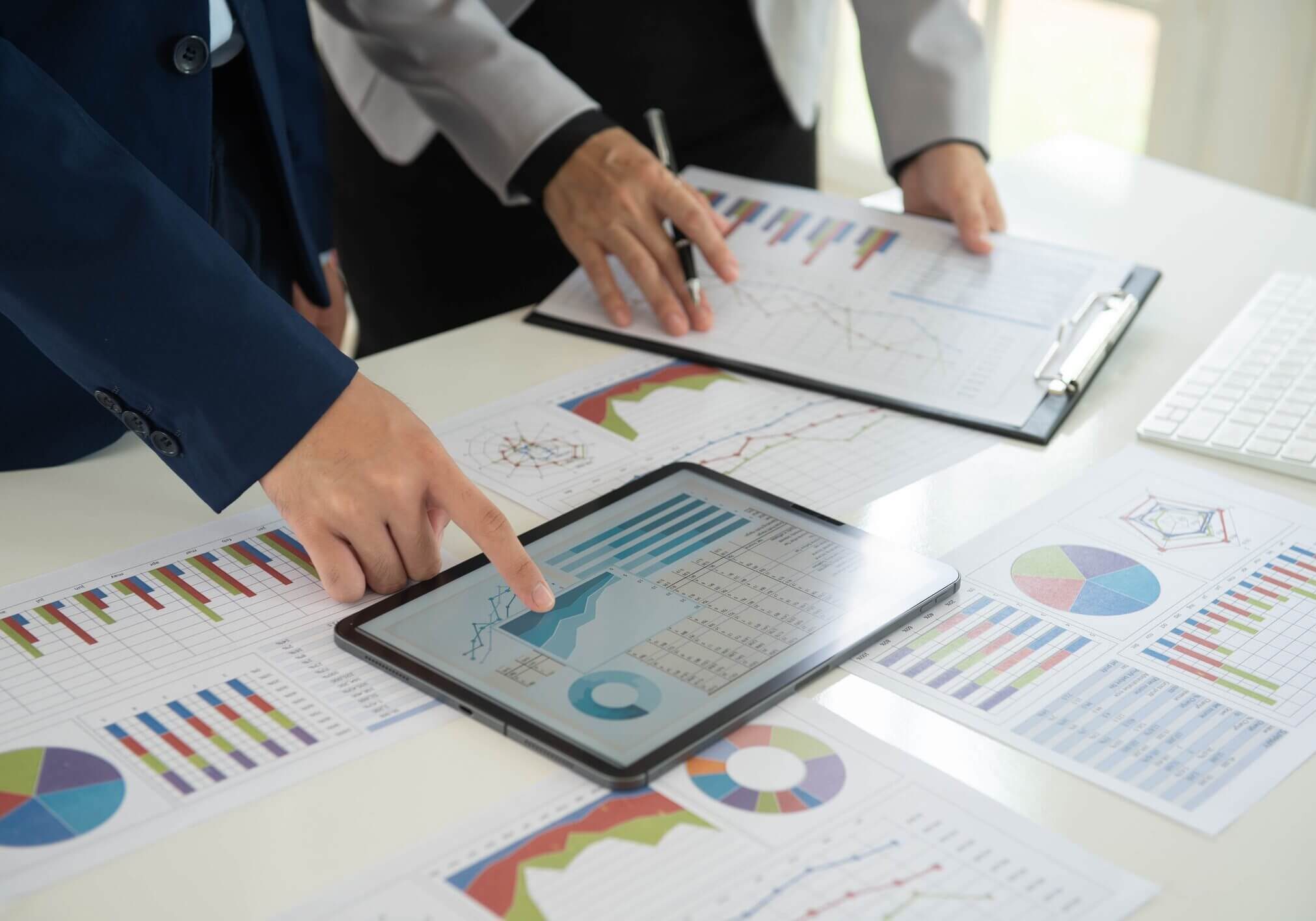 Two business people analyzing charts and graphs on a tablet and printed documents.